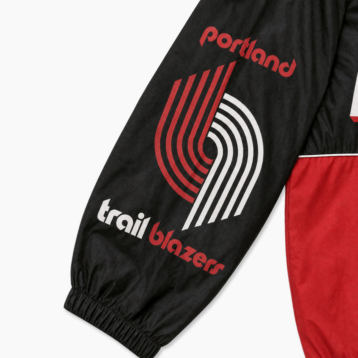 Close-up of a black Portland Trail Blazers windbreaker jacket sleeve featuring the red and white team logo and 'trail blazers' text, with a red body panel visible at the side.