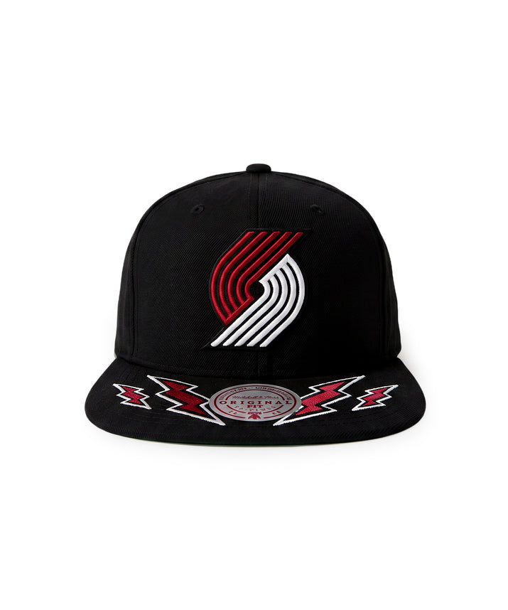 A black flat-brim snapback cap featuring the Portland Trail Blazers logo embroidered on the front in red and white, with red and white lightning bolt embroidery on the brim and a circular Mitchell & Ness brand patch.