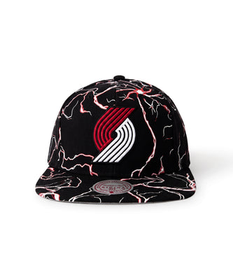 A black flat-brim snapback cap featuring a red and white Portland Trail Blazers logo on the front, decorated with a red and white lightning-bolt pattern across the crown and brim.