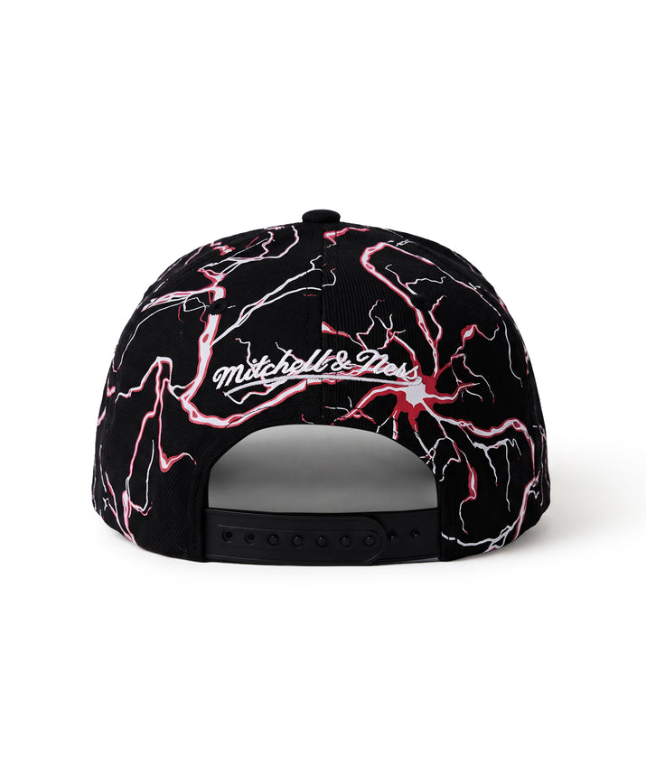 A black snapback cap featuring a vibrant pink and white lightning bolt pattern across the front panels, with the 'Mitchell & Ness' brand logo embroidered in white script across the center.