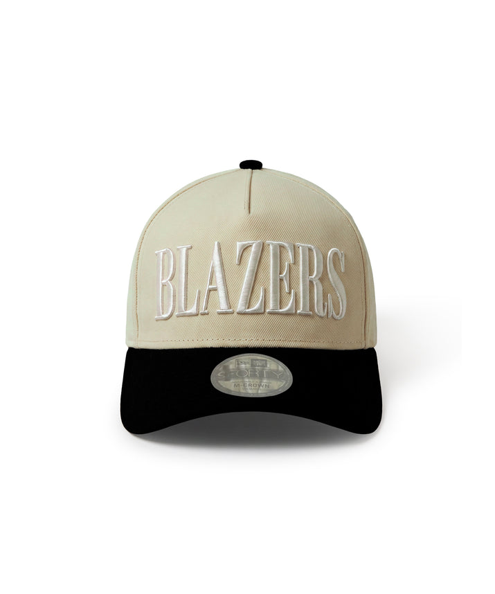 A structured baseball cap with a beige crown and a black curved brim. The word 'BLAZERS' is embroidered in white across the front, and a silver oval sticker is visible on the brim.