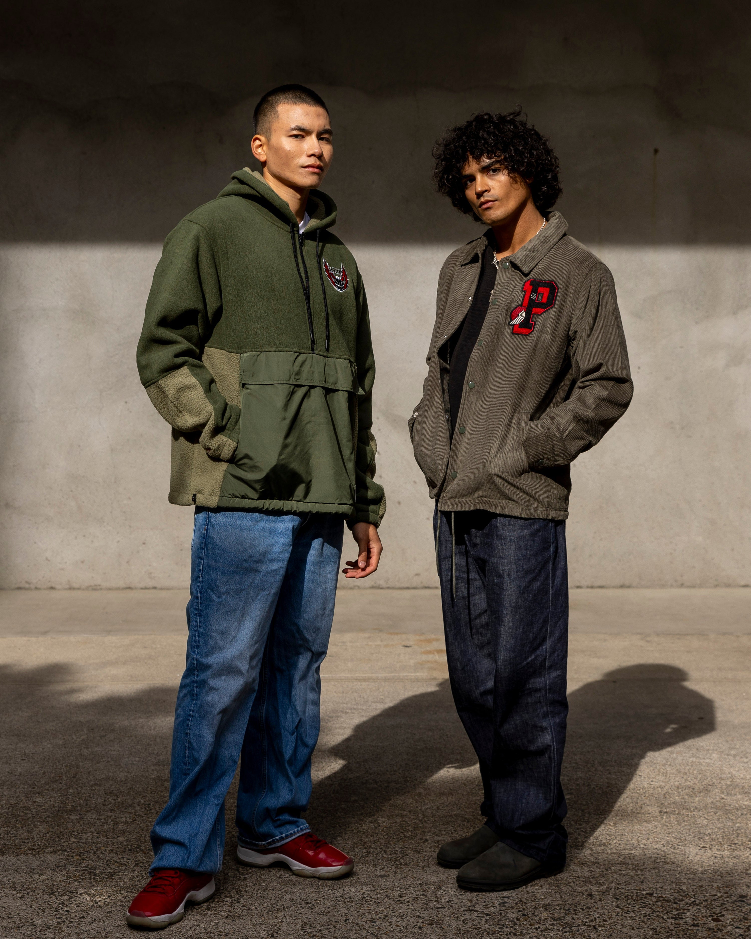 Two men standing side by side against a plain wall.