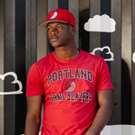Man wearing a red 'Portland' t-shirt standing against a striped wall with cloud graphics.
