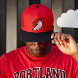 Person wearing a red and black cap with a logo, standing against a striped background.