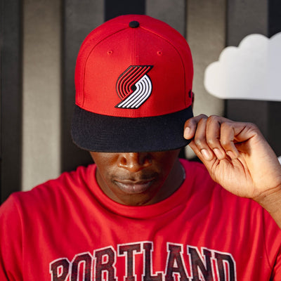 Person wearing a red and black cap with a logo, standing against a striped background.
