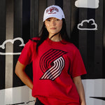 Person wearing a red t-shirt with a logo and a white cap, standing against a black background with cloud and airplane graphics.