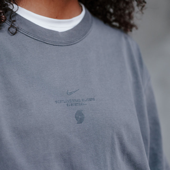 Close-up of a person wearing a faded dark gray Nike sweatshirt with a tonal chest logo, layered over a white crewneck undershirt.