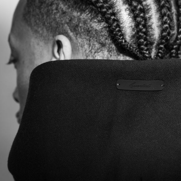 Close-up black fabric neck pillow with a small black leather brand plaque, shown on a person's neck in black and white.
