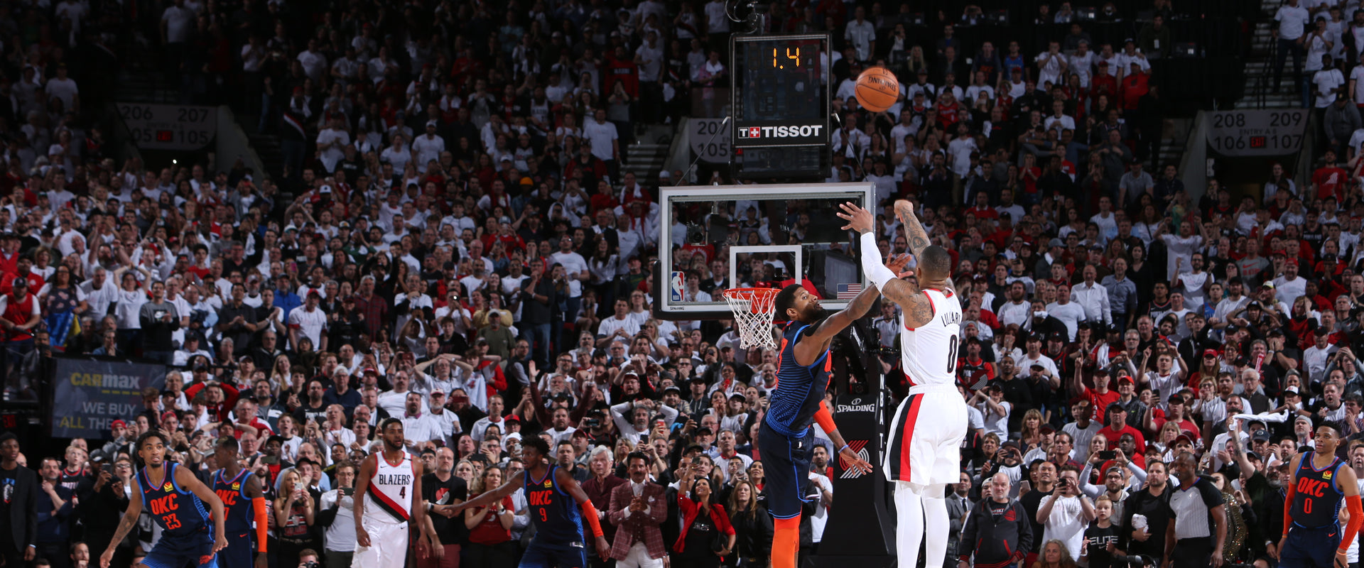 Damian Lillard is in mid-air attempting a shot during a game with a crowd watching.
