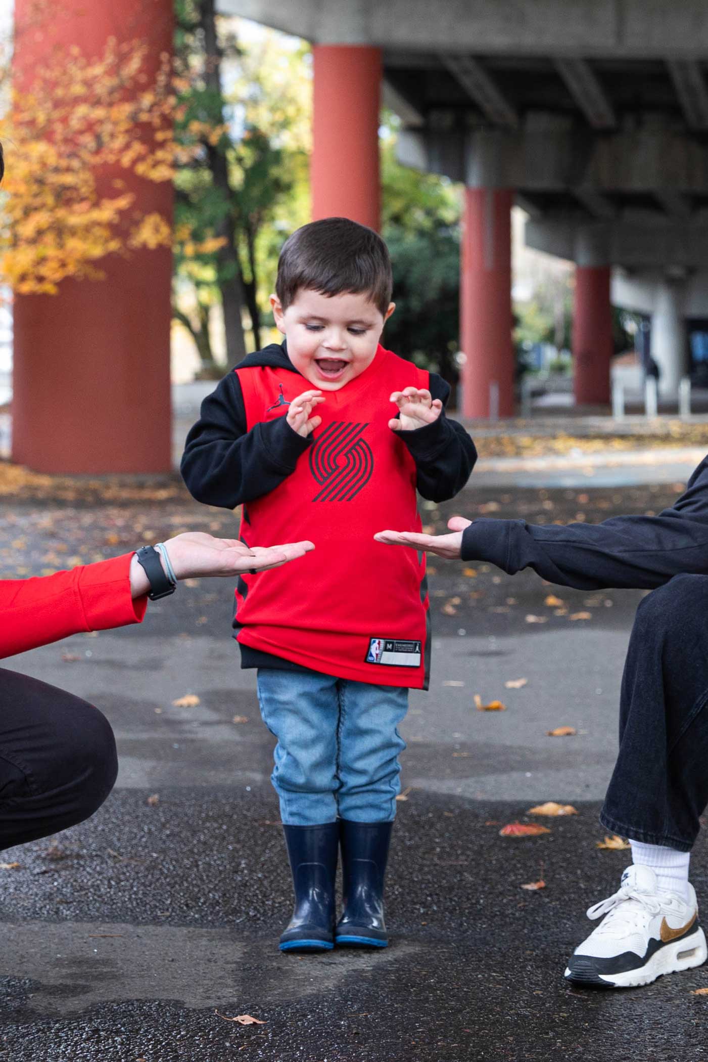 Child wearing Trail Blazers Red Statement Jersey giving high five to parents